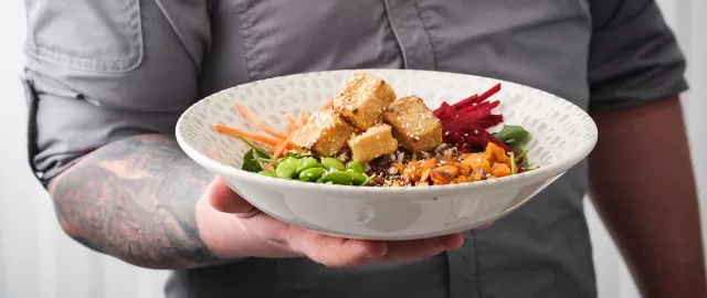 Chef holding bowl of crispy tofu over a bed of mixed vegetables