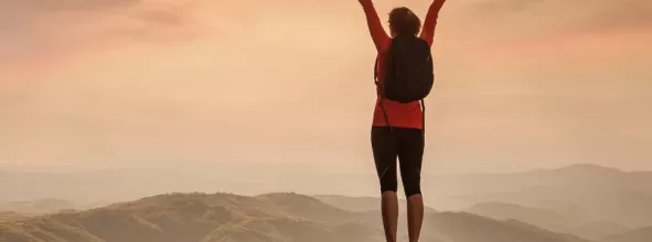 Person holding arms outstretched over head while standing on top of mountain