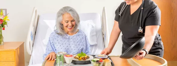 Patient being served a tray of food in hospital bed by assistant