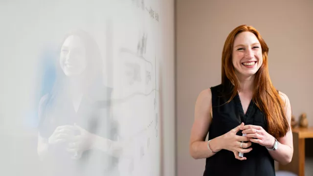 Office employee smiling while standing next to white board