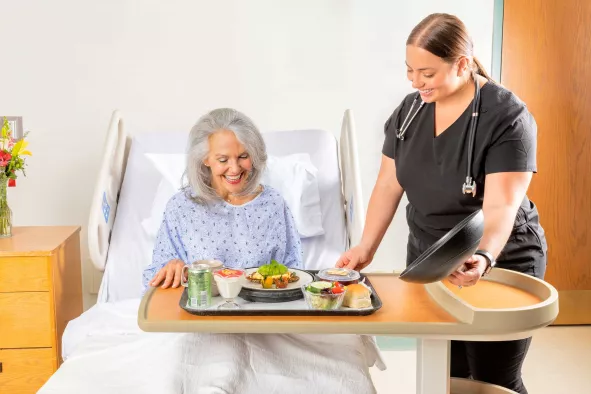 Patient being served a tray of food in hospital bed by assistant