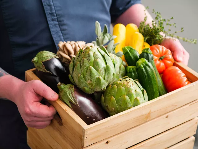 Hands holding wooden crate of vegetables