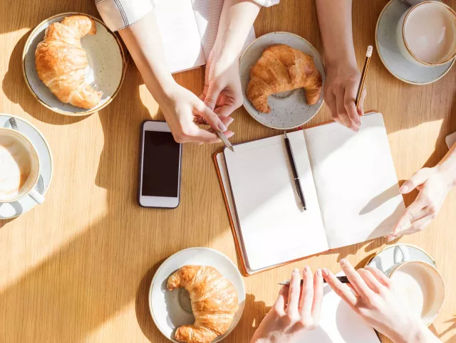 Overhead shot of table with croissants, coffee and hands taking notes